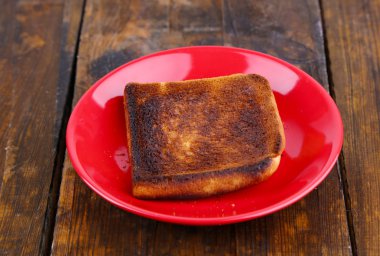Ahşap masa arka plan üzerinde kırmızı plaka üzerinde yanmış tost ekmeği