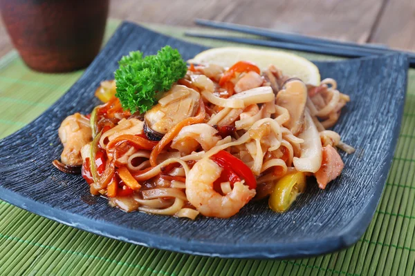 Китайская лапша с овощами и морепродуктами на фоне бамбука — стоковое фото