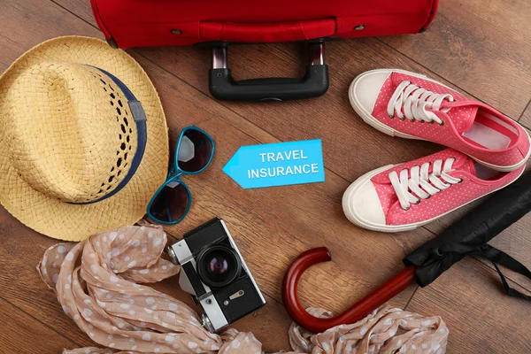Βαλίτσα και τουριστικά πράγματα με επιγραφή ταξιδιωτική ασφάλιση σε ξύλινα φόντο — Φωτογραφία Αρχείου