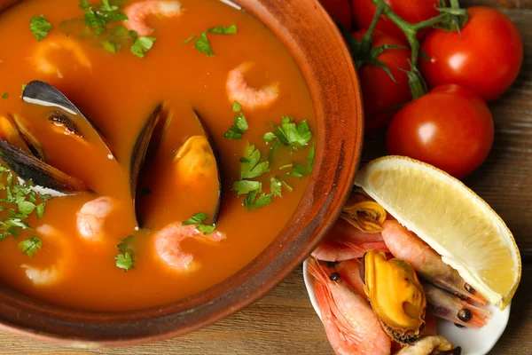 Tasty soup with shrimps, mussels, tomatoes and black olives in bowl on wooden background — Stock Photo, Image