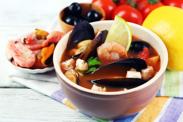 Chutné polévky krevety, mušle, rajčaty a černými olivami v misce na dřevěné pozadí — Stock fotografie