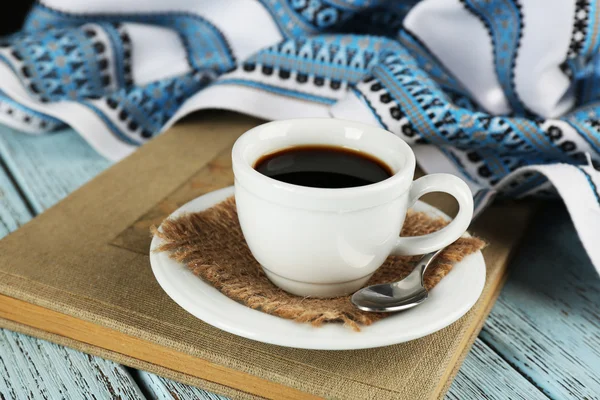 Cup of coffee on book with tablecloth on color wooden background — Stockfoto