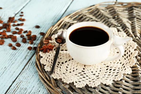 Cup of coffee with lace doily, spoon and coffee beans on wicker stand, on color wooden background — 图库照片