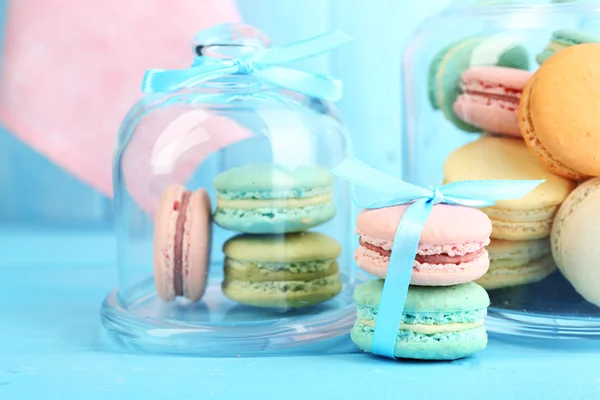 Gentle colorful macaroons in glass jars on color wooden table background — Stock Photo, Image
