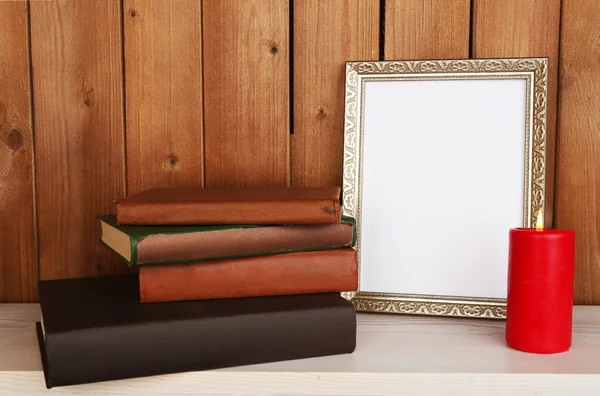 Marco de fotos con vela y libros sobre superficie de madera y fondo de pared de madera — Foto de Stock