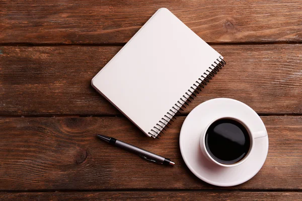 Tasse Kaffee auf Untertasse mit Notizbuch und Stift auf Holztischhintergrund — Stockfoto
