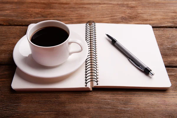 Tasse Kaffee auf Untertasse mit Notizbuch und Stift auf Holztischhintergrund — Stockfoto