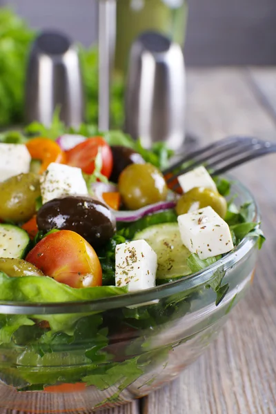 Greek salad in glass dish with fork on wooden table background — Stock Photo, Image