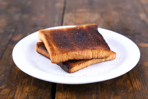 Verbrande toast brood op plaat, op houten tafel achtergrond — Stockfoto