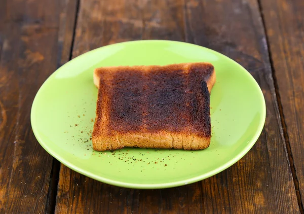 Verbrande toast brood op licht groene plaat, op houten tafel achtergrond — Stockfoto