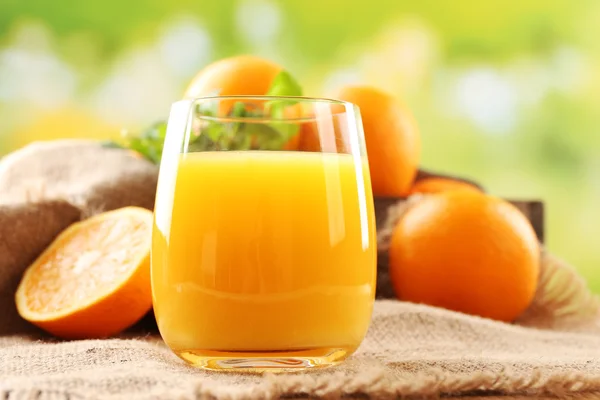 Glass of orange juice on wooden table with burlap cloth and bright background — Stock Photo, Image