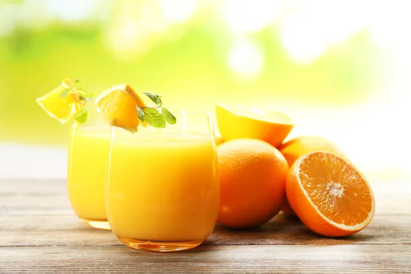 Vaso de zumo de naranja y rebanadas sobre mesa de madera y fondo brillante — Foto de Stock