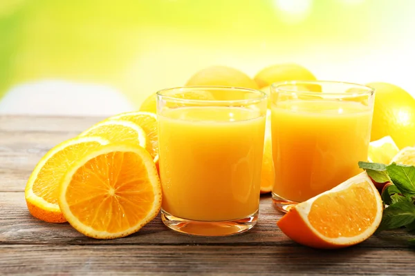 Copo de suco de laranja e fatias na mesa de madeira e fundo brilhante — Fotografia de Stock
