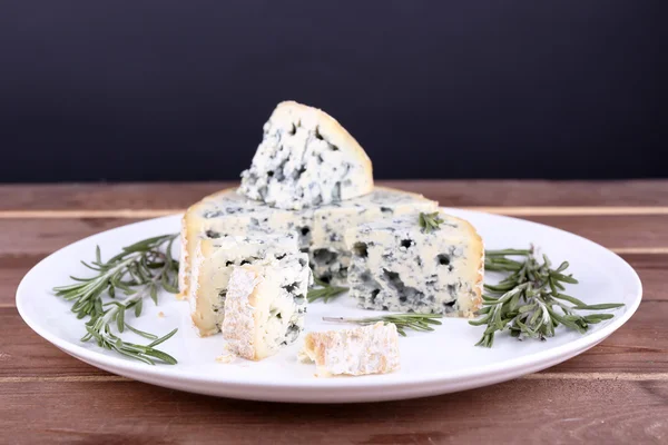 Queso azul con ramitas de romero en plato sobre mesa de madera y fondo oscuro — Foto de Stock