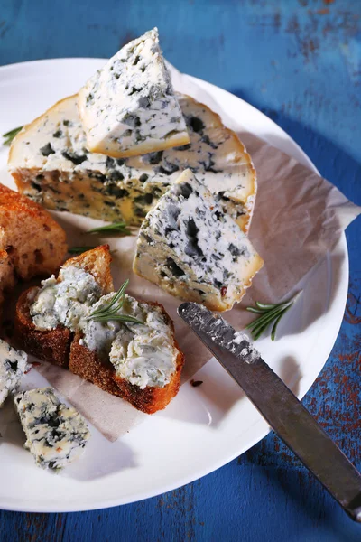 Blue cheese with sprigs of rosemary, bread and nuts on plate and color wooden table background — Stock Photo, Image