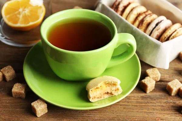 Bunte Makronen mit Tasse Tee auf hölzernem Hintergrund — Stockfoto