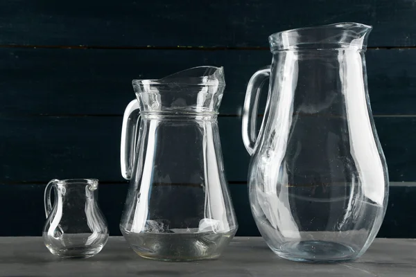 Glass jugs on dark color wooden background — Stock Photo, Image