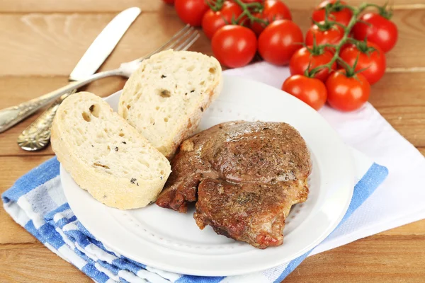 Roasted meat and vegetables on plate, on wooden table background — Stock Photo, Image