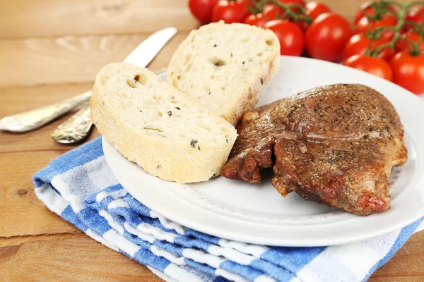 Roasted meat and vegetables on plate, on wooden table background — Stock Photo, Image