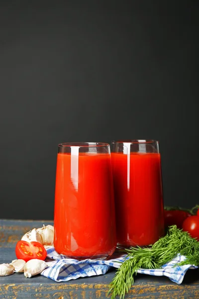 Copos de suco de tomate saboroso e tomates frescos na mesa, no fundo cinza — Fotografia de Stock