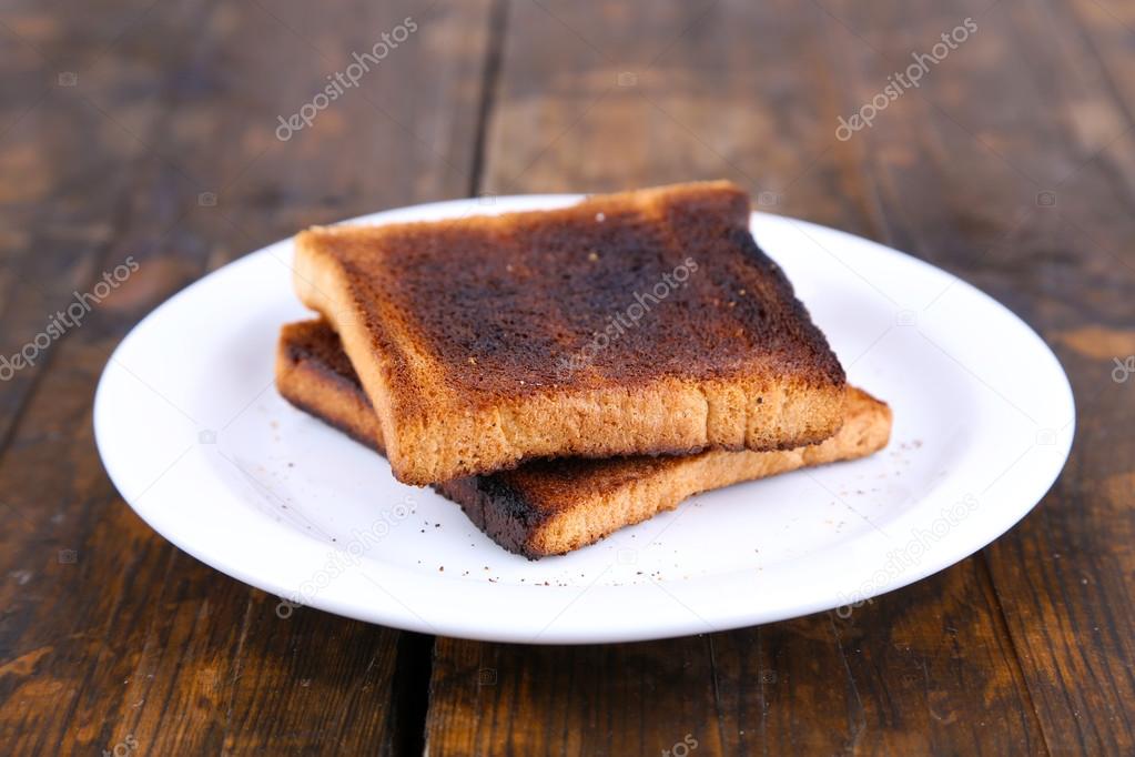 Burnt toast bread on plate, on wooden table background