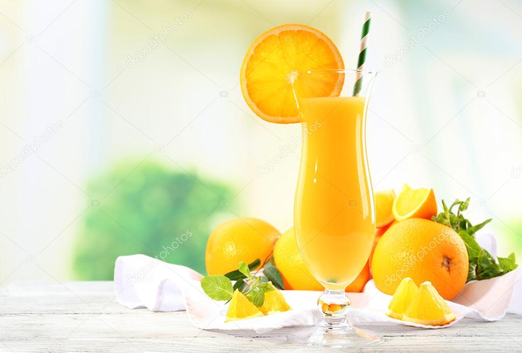Glass of orange juice with straw and slices on wooden table and bright background