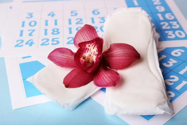Almohadillas sanitarias, calendario y orquídea lila sobre fondo azul claro — Foto de Stock