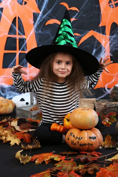 Kleines Mädchen Hexe in Hut mit Kürbissen auf halloween-Dekorationen Hintergrund — Stockfoto