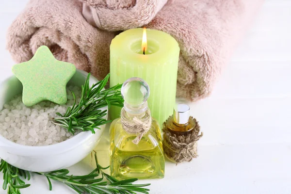 Branches of rosemary and sea salt, towels, candle and bottle with massage oil on color wooden background. Rosemary spa concept — Stock Photo, Image