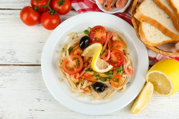 Tasty pasta with shrimps, black olives and tomato sauce on plate on wooden background — Stock Photo, Image