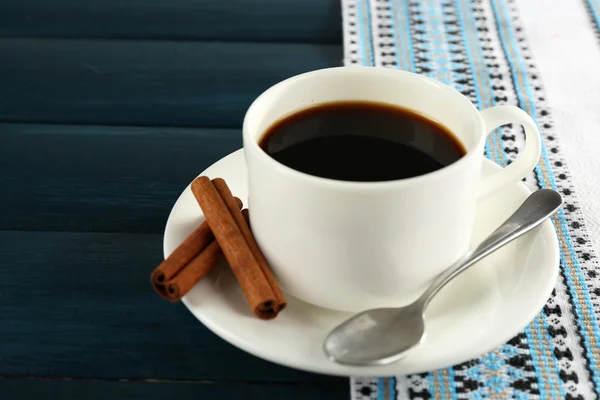 Taza de café con canela y cuchara sobre mantel, sobre fondo de madera de color — Foto de Stock