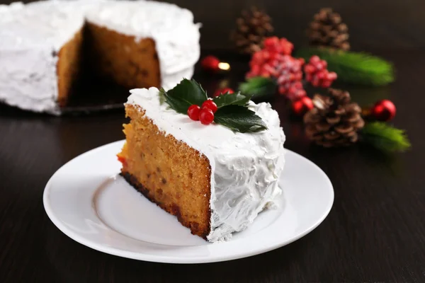 Кусок торта, покрытый сливками с рождественским декором на фоне деревянного стола — стоковое фото