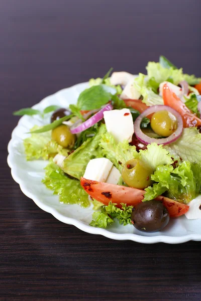 Griekse salade in plaat op houten ondergrond — Stockfoto