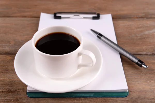 Tasse de café sur soucoupe avec feuille de papier et stylo sur fond de table en bois — Photo