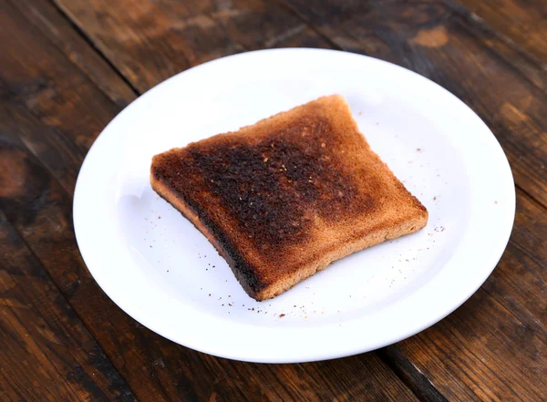 Burnt toast bread on plate, on wooden table background — Stock Photo, Image