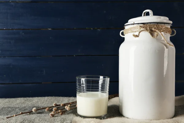 Milchkanne und Glas auf farbigem Holzhintergrund — Stockfoto