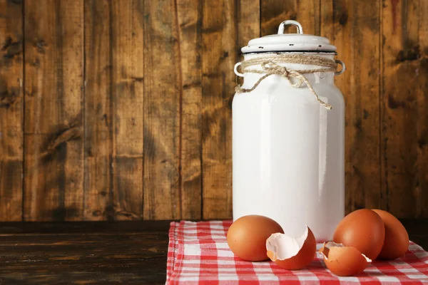 Melk kan met eieren en de "eggshell" op servet op rustieke houten achtergrond — Stockfoto