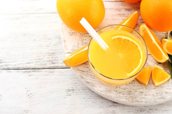 Copo de suco de laranja com palha e fatias em fundo de mesa de madeira — Fotografia de Stock