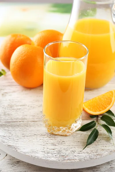 Glass of orange juice and oranges on color wooden table background — Stock Photo, Image