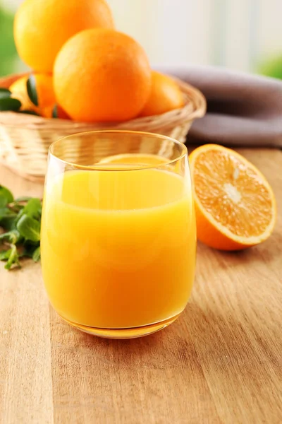 Стекло апельсинового сока и плетеная корзина с апельсинами на деревянном столе и яркий фон — стоковое фото