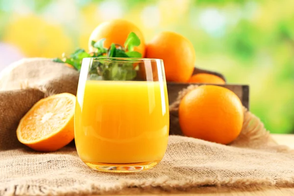 Склянка апельсинового соку на дерев'яному столі з тканиною мішковини і яскравим фоном — стокове фото