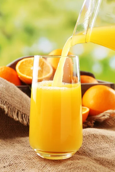 Pouring orange juice from glass carafe, on wooden table and bright background — Stock Photo, Image