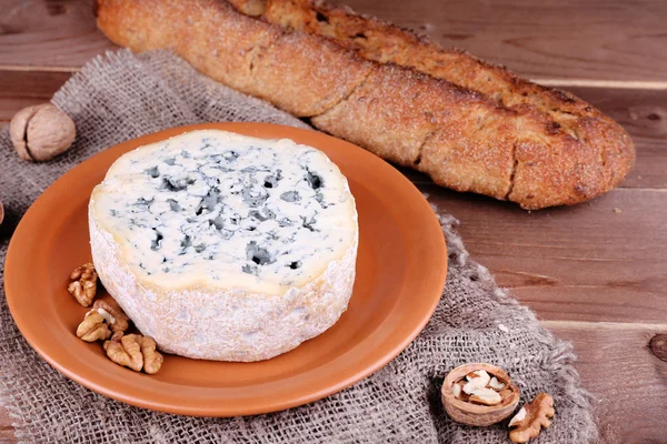 Queso azul sobre plato de barro con nueces y baguette sobre tela de arpillera y fondo de mesa de madera — Foto de Stock