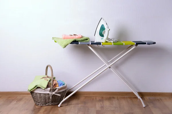 Ironing board with laundry on light background — Stock Photo, Image