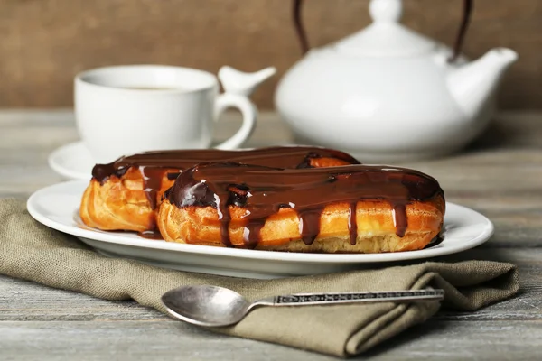 Tasty eclairs and cup of tea on wooden table — Stock Photo, Image