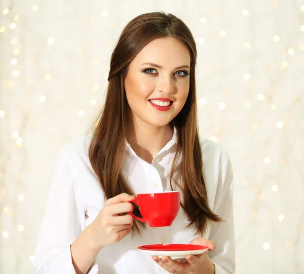 Chica sonriente con taza de bebida caliente sobre fondo de luces —  Fotos de Stock