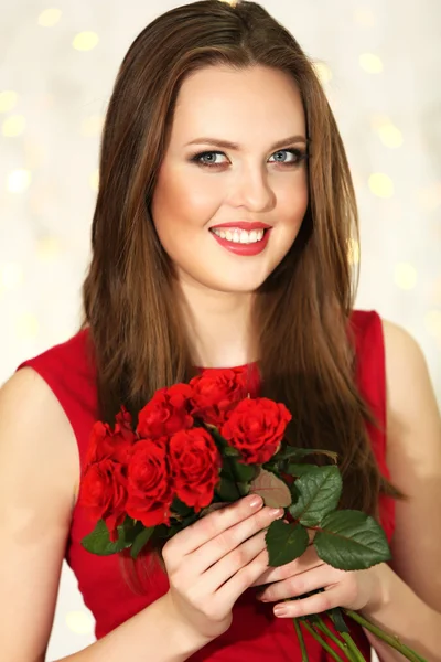 Smiling girl with bouquet of red roses on lights background — Stock Photo, Image