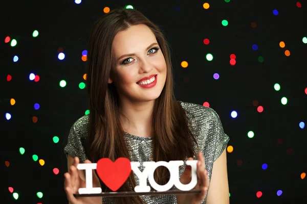 Smiling girl  holding decorative wooden inscription on lights background — Stock Photo, Image