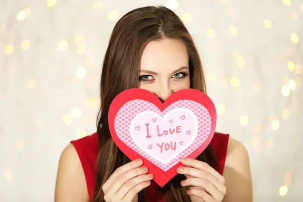 Lächelndes Mädchen mit Valentinskarte mit Grüßen auf Lichterhintergrund — Stockfoto