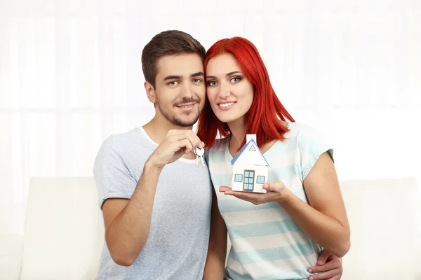 Loving couple sitting in sofa and holds toy house and keys — Stock Photo, Image